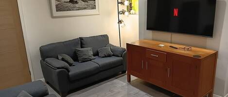 En stue med en grå sofa, et træskab, et fladskærms-tv og et billede i ramme på væggen.