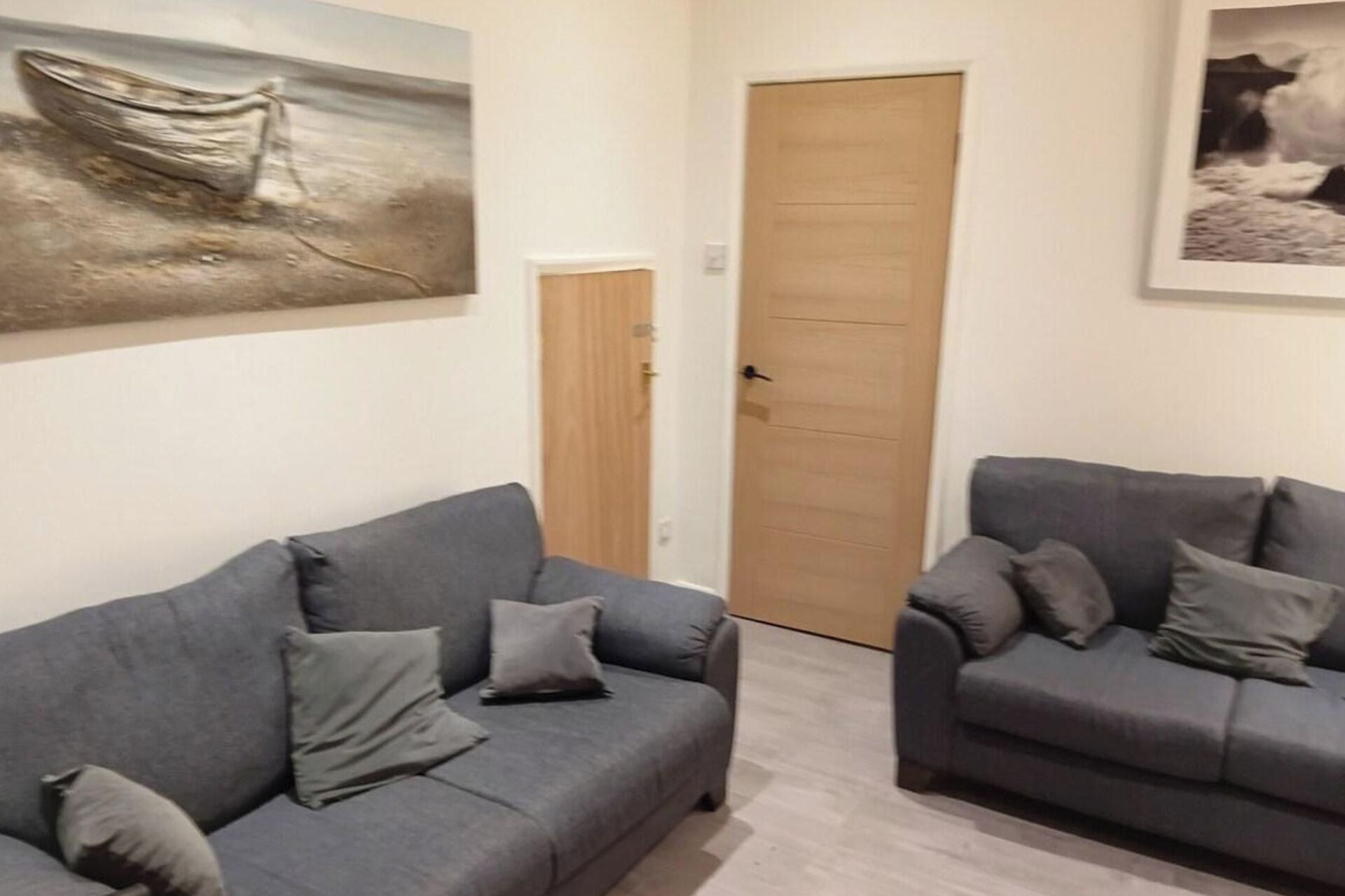 Ein Zimmer mit zwei grauen Sofas, einer Holztür und zwei Bildern an den Wänden.