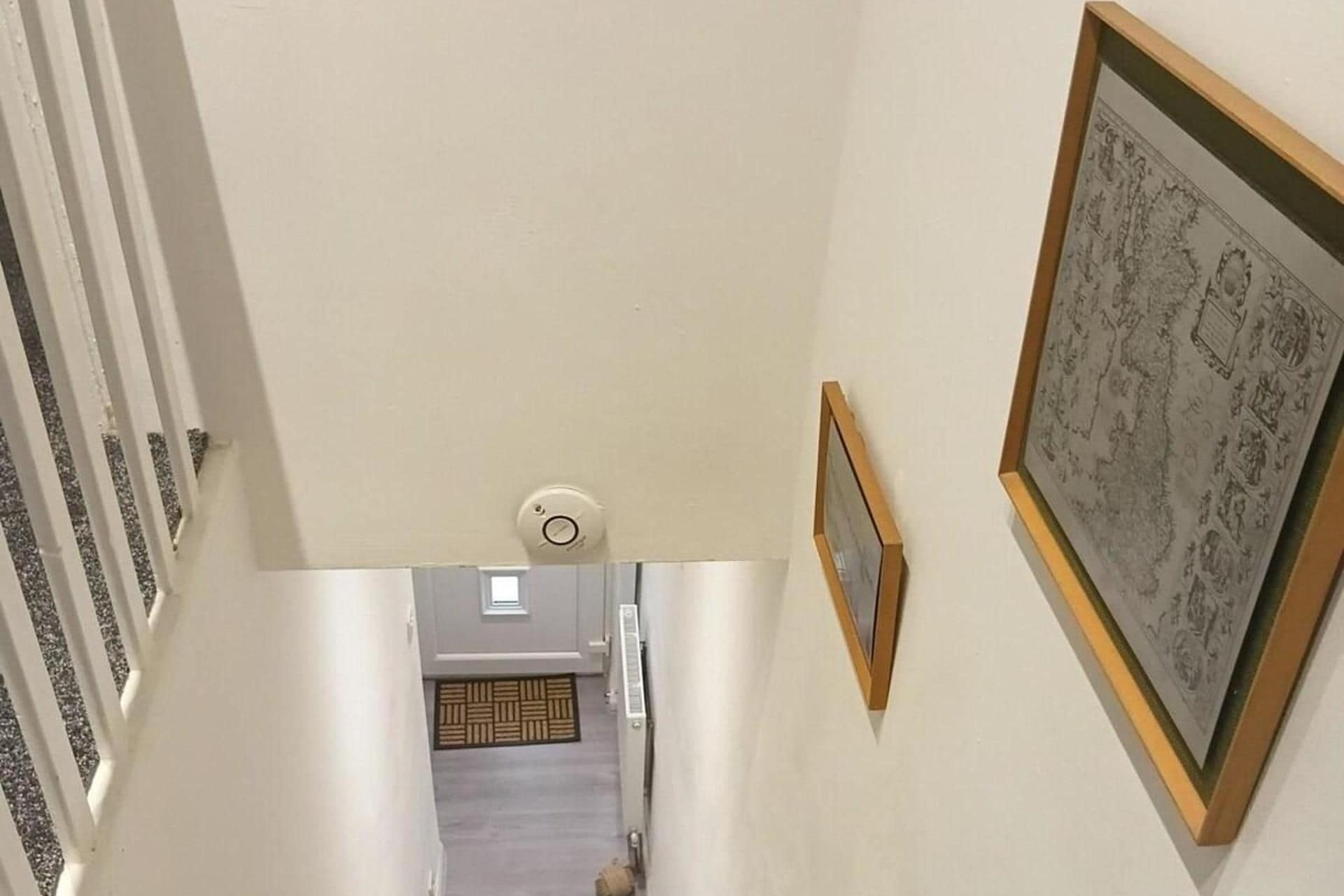 En gang med loftlampe, radiator og et billede i ramme på væggen.