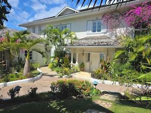 Une maison dotée d’un porche abrité, entourée d’une végétation tropicale luxuriante et d’un jardin bien entretenu.