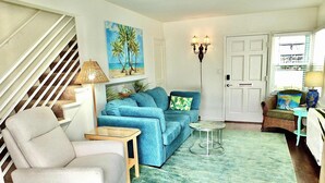 A living room with a staircase, a blue sofa, a white armchair, a small table, and a floor lamp. - Walk to Beach, Tropical Patio, World Cup, Sleeps 5 (Long Beach)