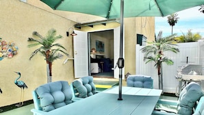 An outdoor patio with a table and chairs, surrounded by palm trees and a decorative wall. - Walk to Beach, Tropical Patio, World Cup, Sleeps 5 (Long Beach)