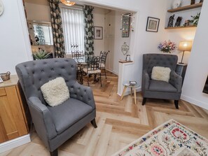 A living room with two grey armchairs, a dining table with chairs, a small side table, and a patterned rug. - Sea Mist (Newbiggin-by-the-Sea)