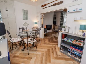 Een eethoek met een ronde glazen tafel en stoelen, een boekenkast met gezelschapsspellen, een open haard en een televisie op de achtergrond.