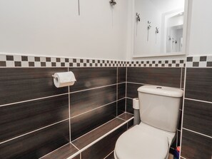 Een badkamer met donkere betegelde wanden, een toilet en een zeepdispenser.