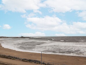 Een kuststrand met golven, een rotsachtige kustlijn en een gebouw in de verte.