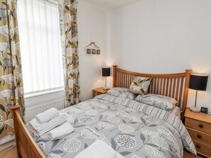 Een slaapkamer met een bed, twee nachtkastjes, een wandlamp, een radiator en een raam met gordijnen.