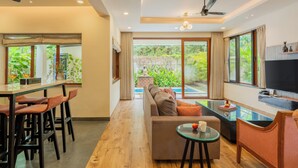 Una sala de estar moderna con un sofá, un comedor con sillas, un televisor y vistas a áreas verdes.