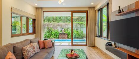 A living room with a sofa, coffee table, TV, and a view of a swimming pool.