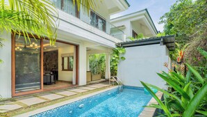 Una casa moderna con piscina, grandes puertas correderas de vidrio y abundante follaje.