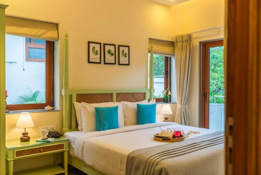 A hotel room with a bed, bedside tables, a window, and a view of greenery outside.