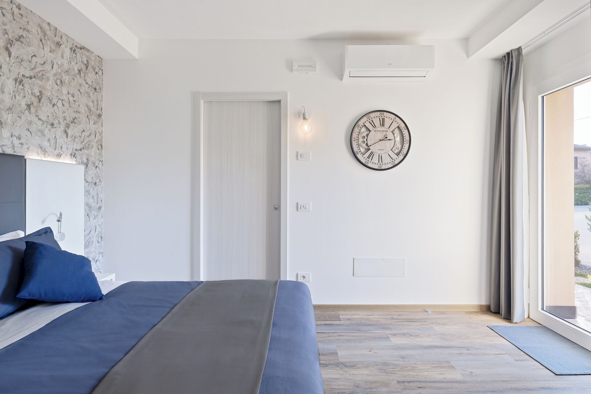 Une chambre à coucher avec un lit, une horloge murale, une porte et une fenêtre.