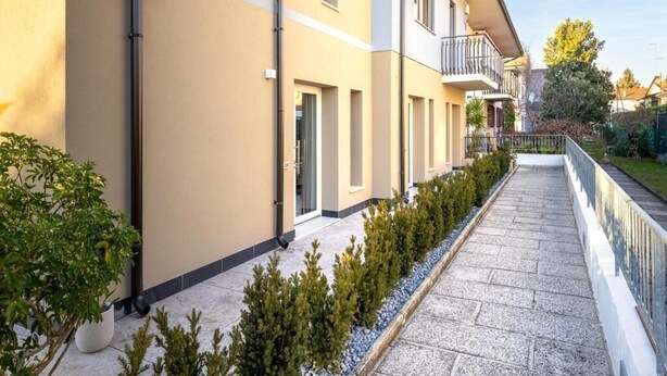 Un immeuble résidentiel à plusieurs étages, doté d’un chemin piétonnier pavé, de plantes en pot et d’une rambarde.