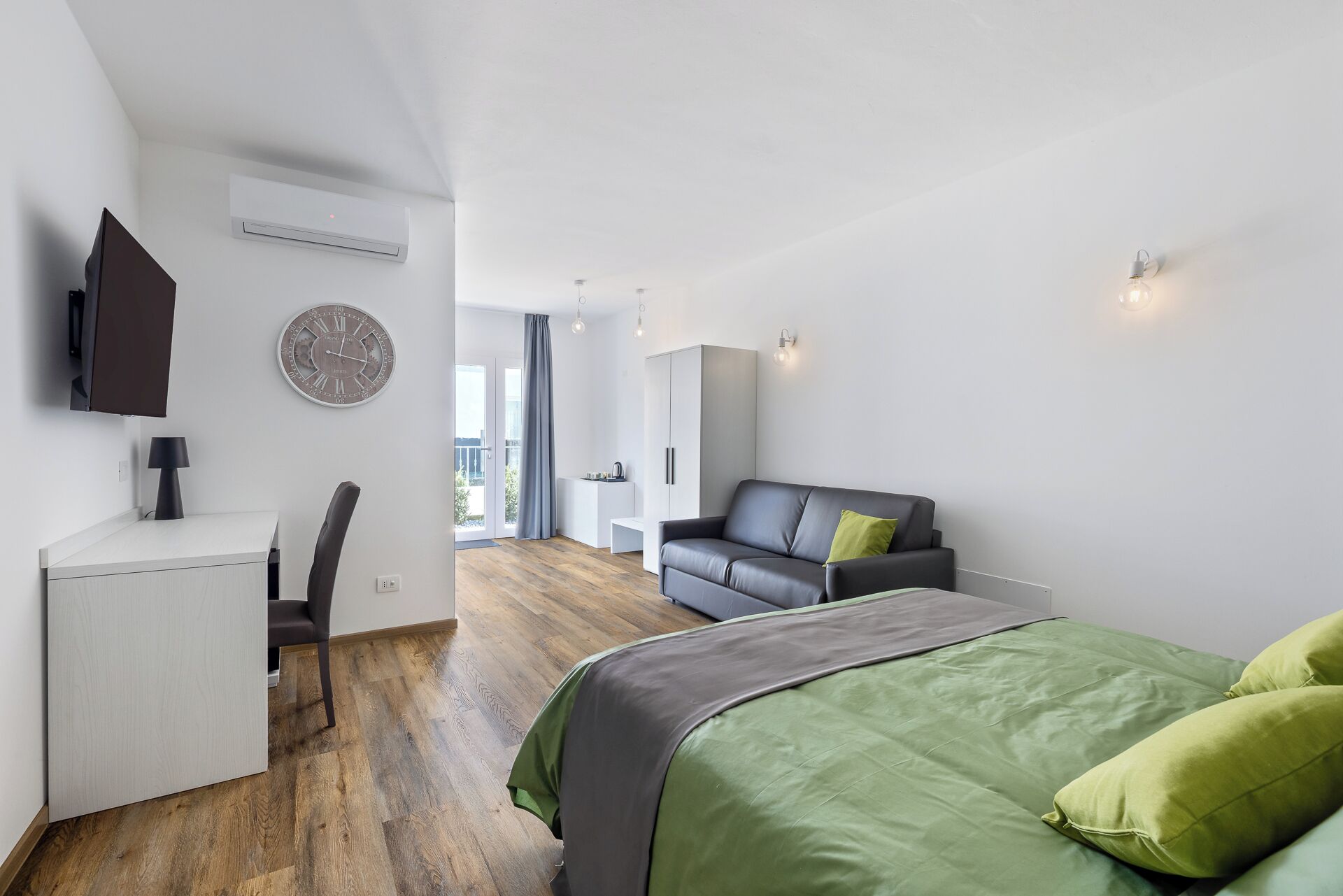 Un dormitorio moderno con cama, escritorio, sillón, sofá y vistas al exterior.