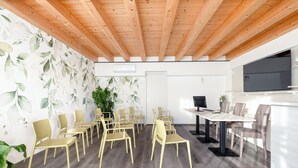 Une salle de conférence avec des poutres en bois au plafond, une grande plante et un téléviseur fixé au mur.