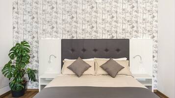 A bedroom with a tufted headboard, a large bed with two pillows, a bedside table, and a potted plant.
