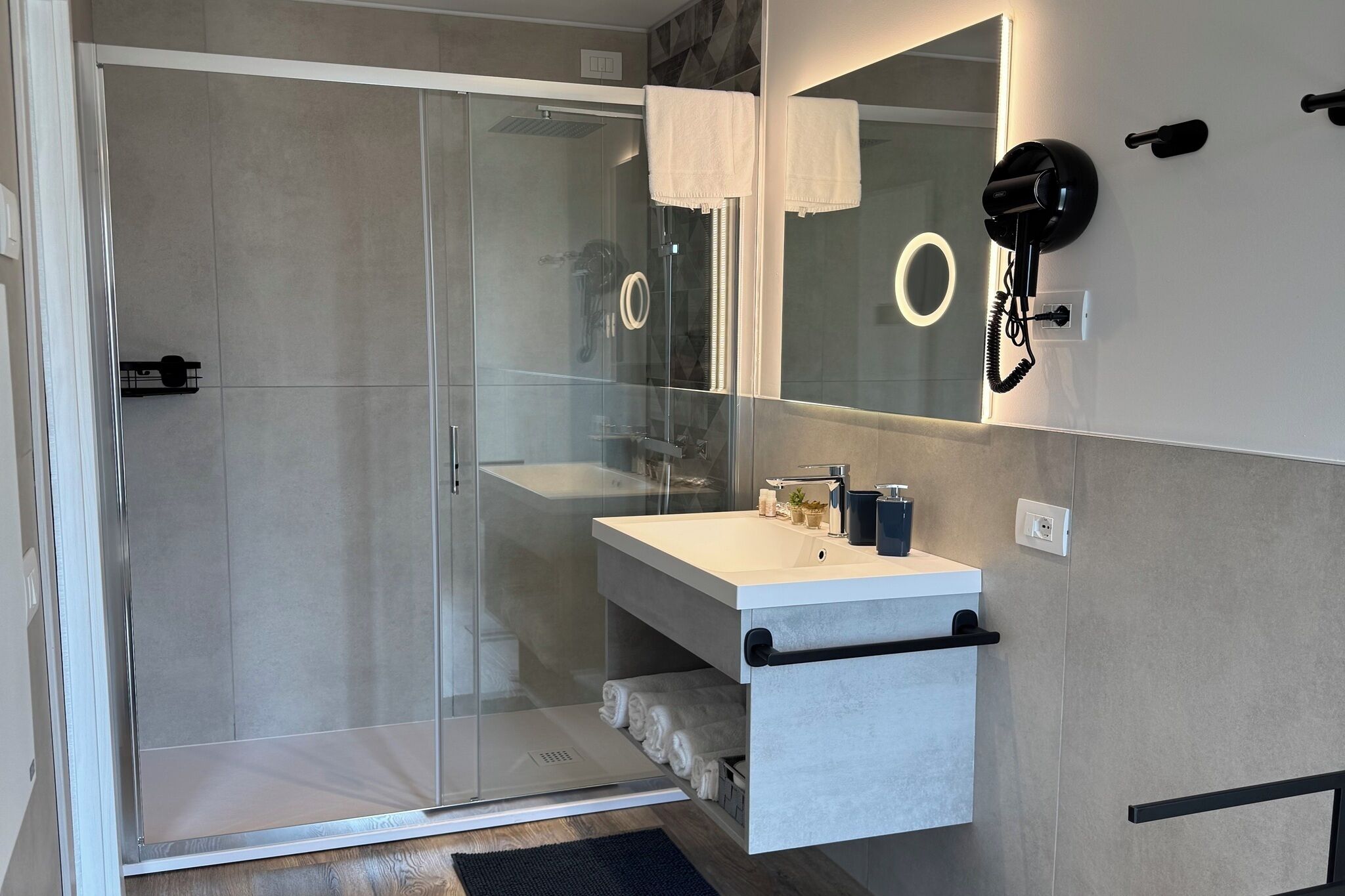 Un bagno moderno con doccia vetro, un mobile lavabo bianco con specchio e un portasciugamani.