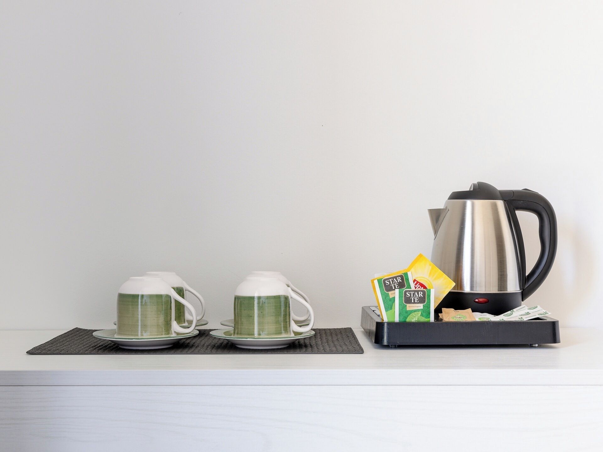 A kitchen counter with two white mugs, a black electric kettle, and a box of tea bags.