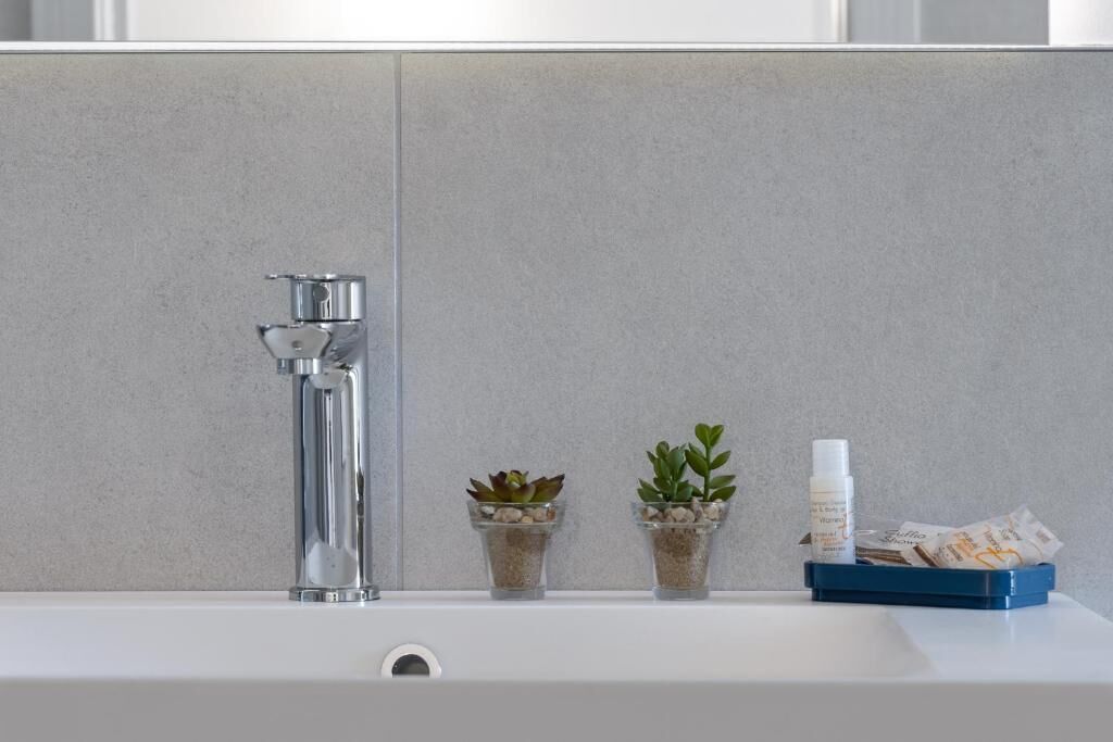 A bathroom with a white sink, a chrome faucet, two small potted plants, and a blue tray with toiletries.