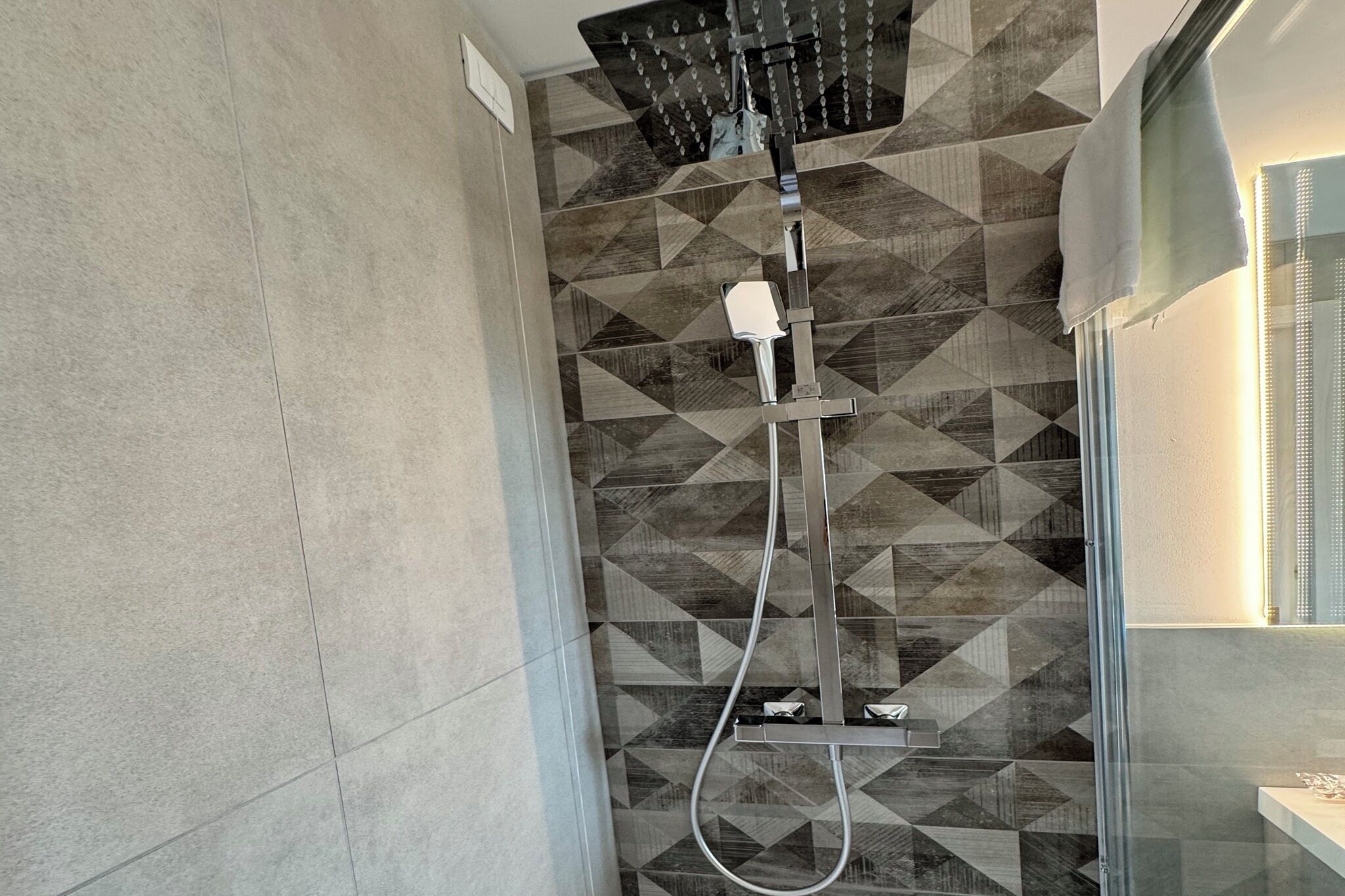A shower with a modern design, geometric patterned wall tiles, and a glass enclosure.