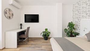 Une chambre à coucher avec un lit, un bureau avec une chaise, une télévision et deux plantes en pot.