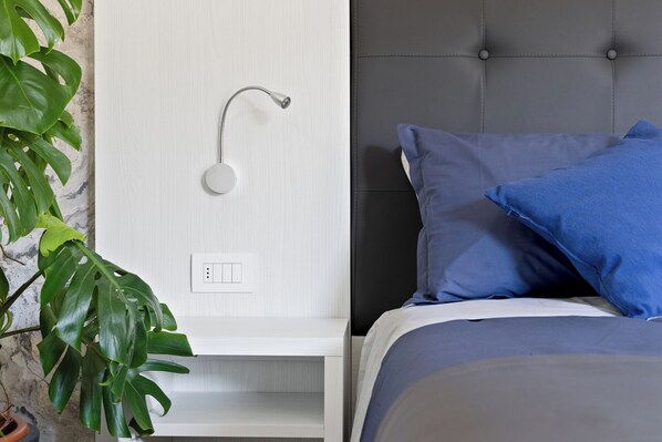 A bedroom with a bed, a nightstand, a wall-mounted shower, and a potted plant.