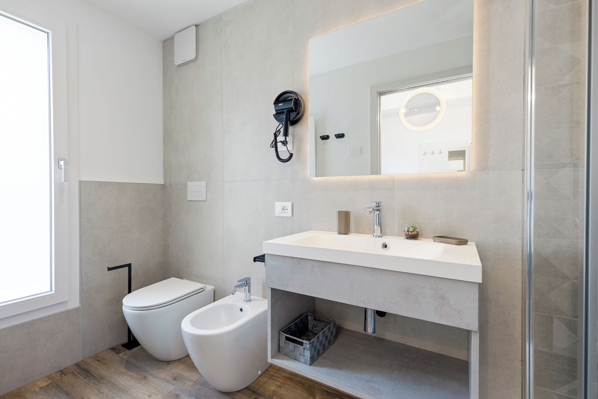 Un baño moderno con inodoro, bidé y lavamanos, secador de pelo y espejo con luz.