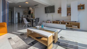 Ein modernes Wohnzimmer mit Fernseher, einer Couch, einem Couchtisch und einer Küche im Hintergrund.