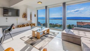 Ein modernes Wohnzimmer mit einer Couch, einem Couchtisch, einem Fernseher und einem großen Fenster mit Meerblick.