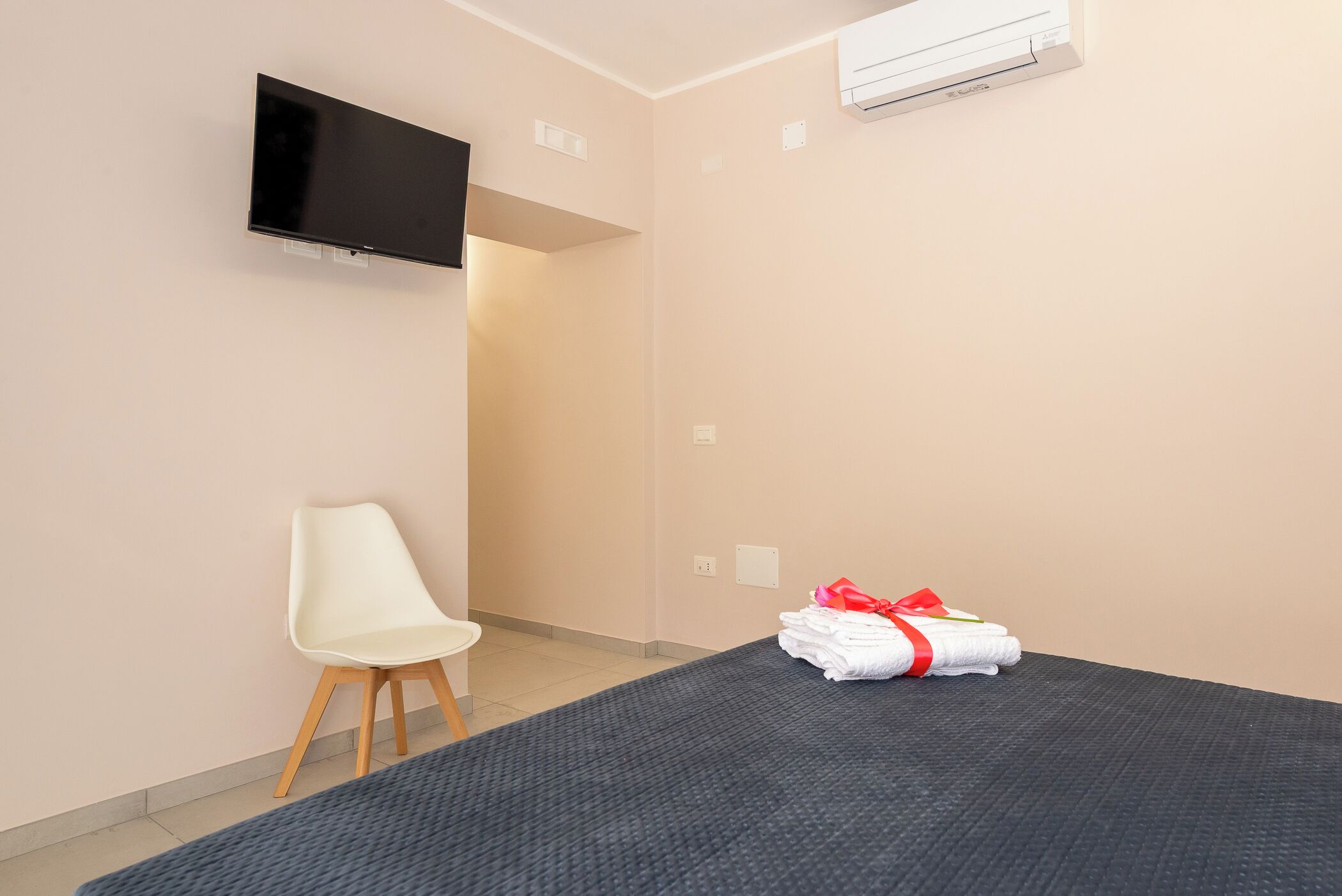 Habitació d'hotel amb llit, televisió penjada a la paret, una cadira i una pila de tovalloles.
