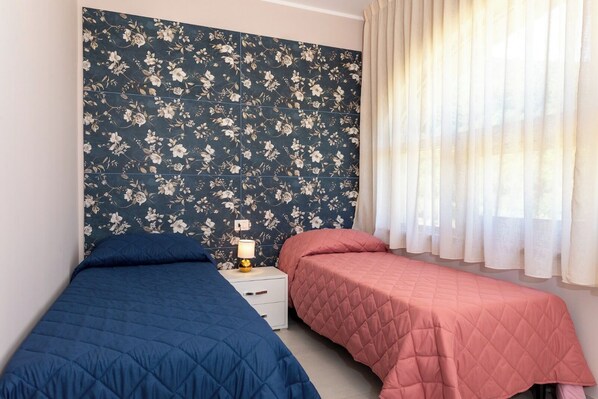 A bedroom with two beds, a nightstand with a lamp, and a window with sheer curtains. - B&B Fonte Silente (Roccadaspide)