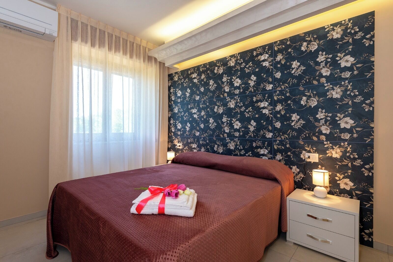 Una camera d'hotel con un letto, un comodino, una lampada e una carta da parati floreale.