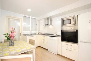 Una cocina moderna con armarios blancos, electrodomésticos de acero inoxidable y una mesa de comedor con mantel estampado.