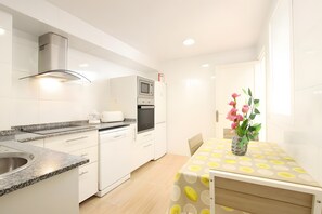 A modern kitchen with white cabinetry, a granite countertop, a built-in microwave, and a dining area with a table and chairs. - Apartment 'Marcos' with Balcony, Wi-Fi and Air Conditioning (Port de Pollença)