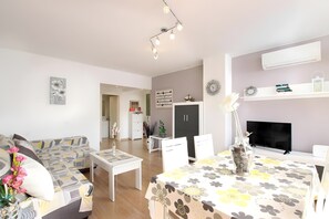 A modern living room with a sofa, dining table, and TV. There is a fireplace, a bookshelf, and a door leading to another room. - Apartment 'Marcos' with Balcony, Wi-Fi and Air Conditioning (Port de Pollença)