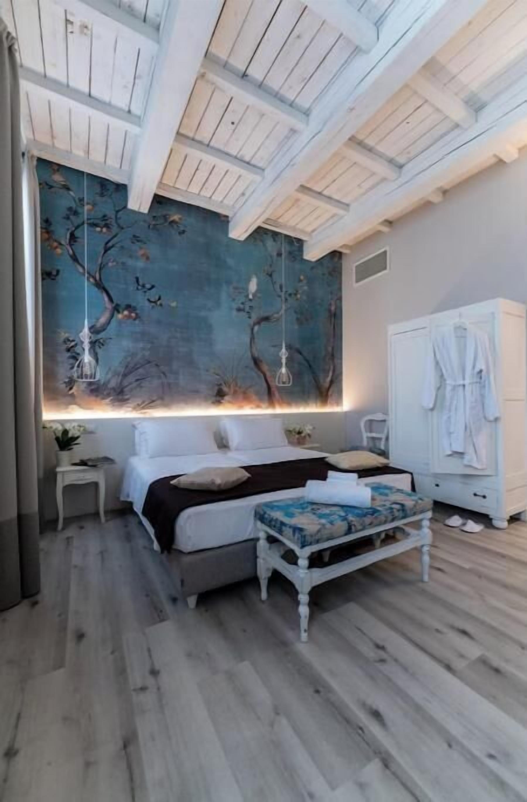 Quarto com cama, mesa de cabeceira, luminária suspensa, guarda-roupa e um grande mural na parede.