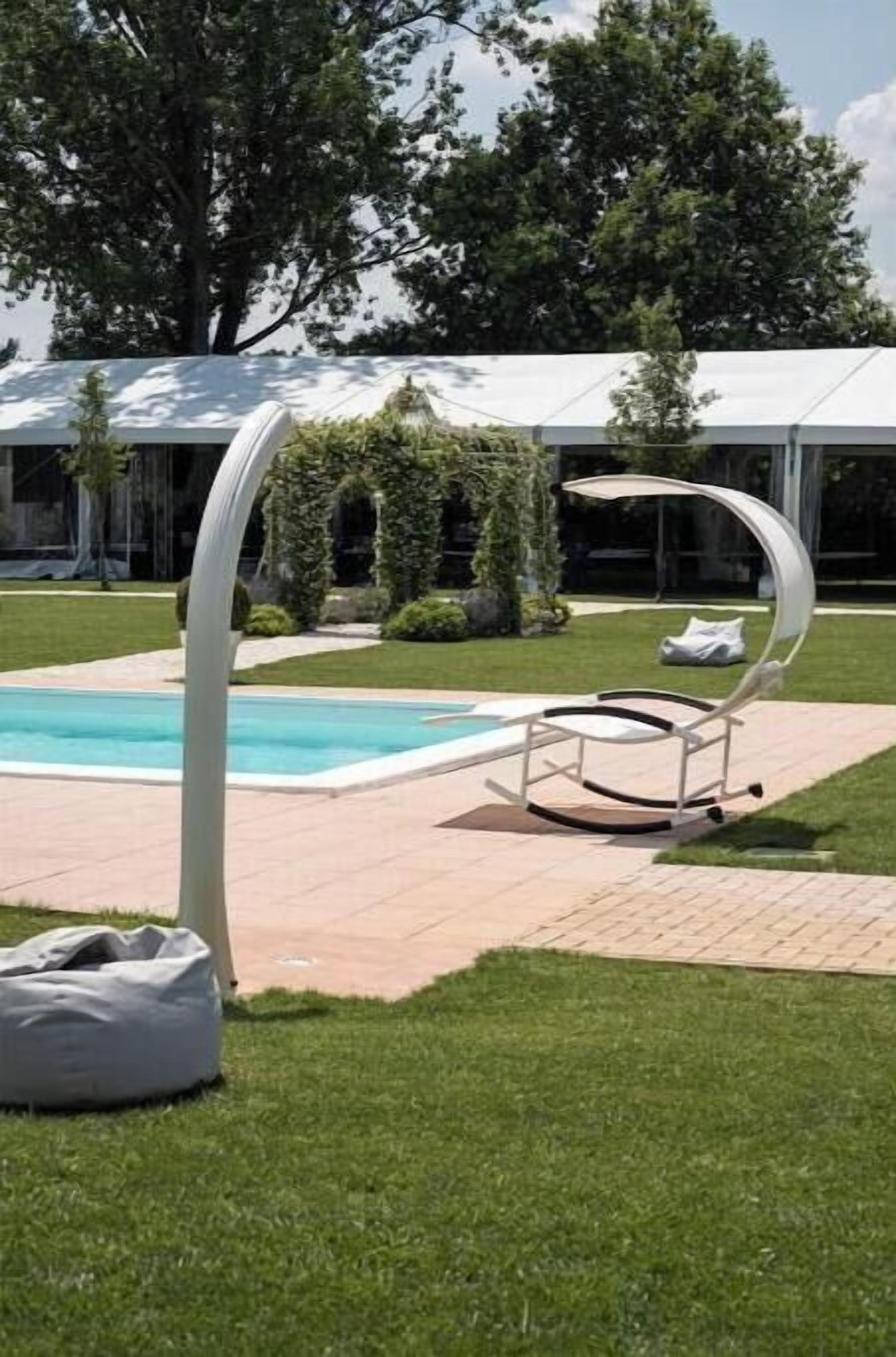 A pool area with a lounge chair, a white tent-like structure, and a grassy lawn.