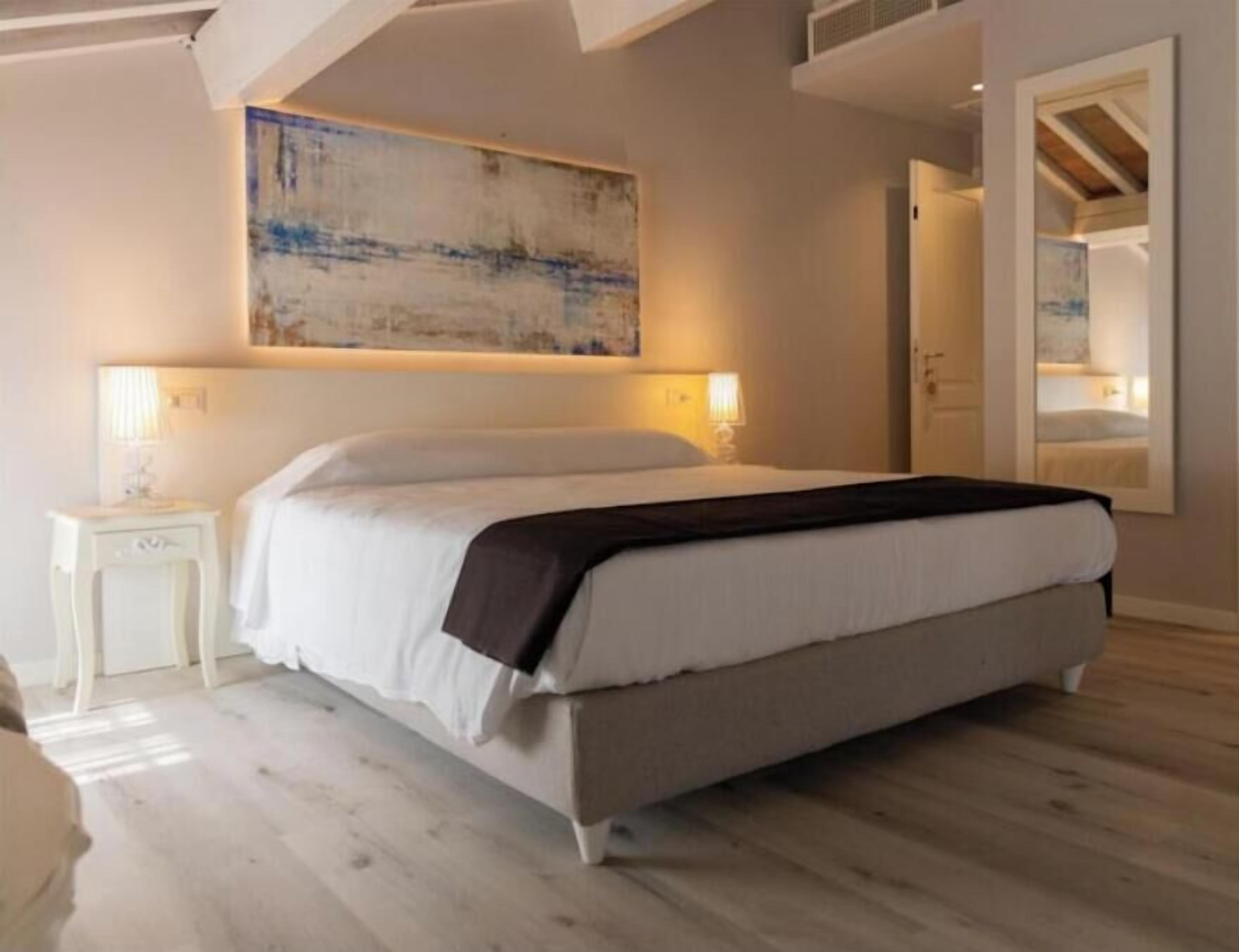 A bedroom with a bed, bedside lamps, a large abstract painting, and a mirror.