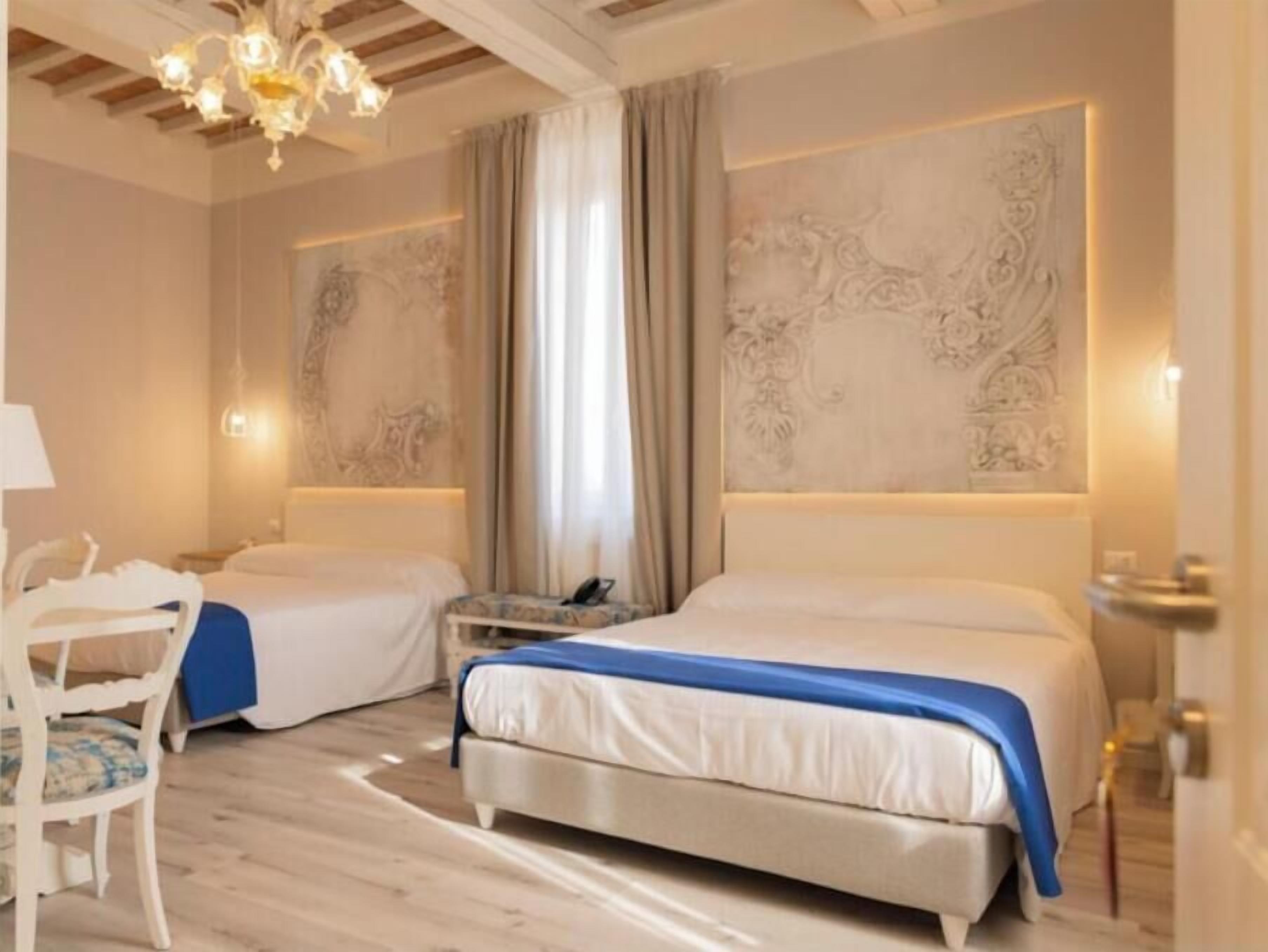 Ein Hotelzimmer mit zwei Betten, einem Schreibtisch, einem Sessel und einer Deckenleuchte.