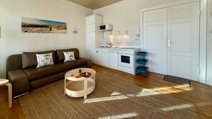 Un espace de vie compact comprenant un canapé, une petite table ronde, un coin cuisine et une porte.