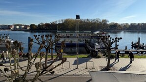 Une promenade au bord de la rivière, avec un bateau amarré au loin, des arbres et un ciel dégagé.