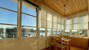 Un espace repas avec des meubles en bois, de grandes fenêtres et une vue sur un plan d’eau.