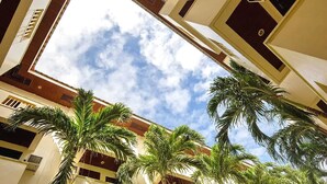 A high-ceiling atrium with a view of the sky, palm trees, and a building facade with windows and air conditioning units. - Palette Boracay Isle by The White Beach (Boracay Island)