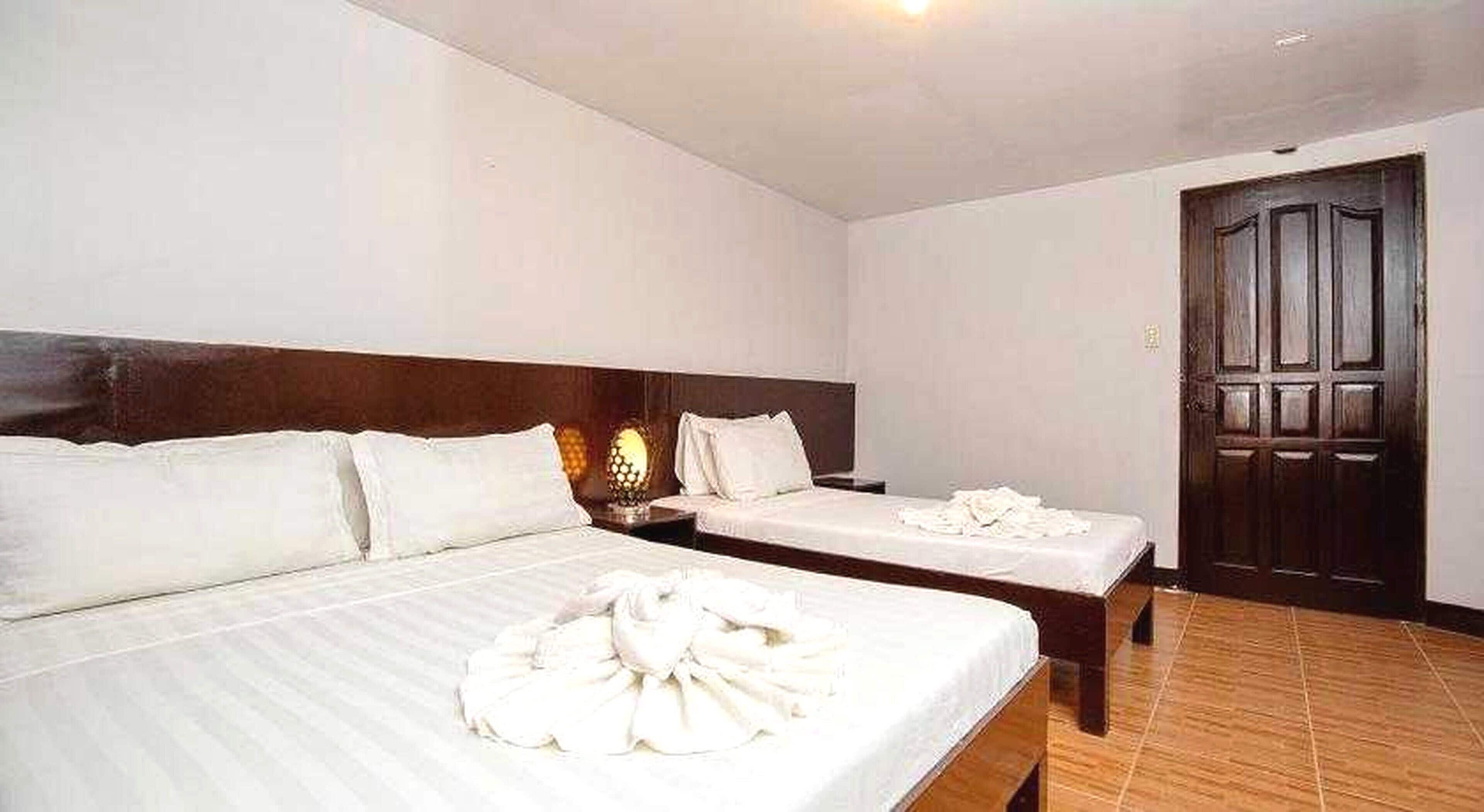 Une chambre d’hôtel avec deux lits, une tête de lit en bois, une table de chevet avec une lampe et une porte en bois foncé.