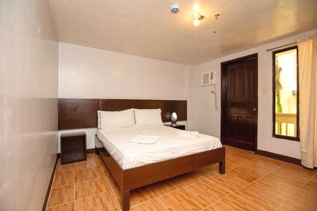 Un dormitorio con una cama de madera, una mesita de noche, una ventana con cortinas y una puerta.