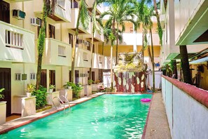 A pool area with a water feature, surrounded by multi-story buildings with balconies and air conditioning units. - Palette Boracay Isle by The White Beach (Boracay Island)