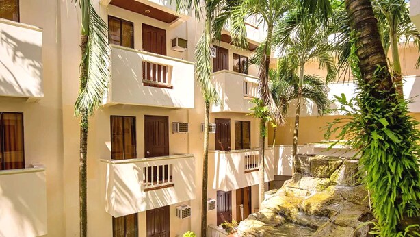 A multi-story hotel with balconies, a water feature, and tropical plants. - Palette Boracay Isle by The White Beach (Boracay Island)