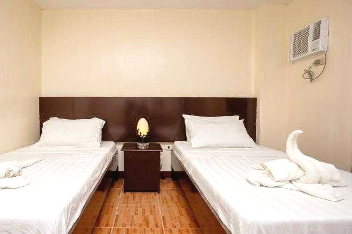 Habitación de hotel con dos camas, una mesita de noche, una lámpara y un aire acondicionado de pared.