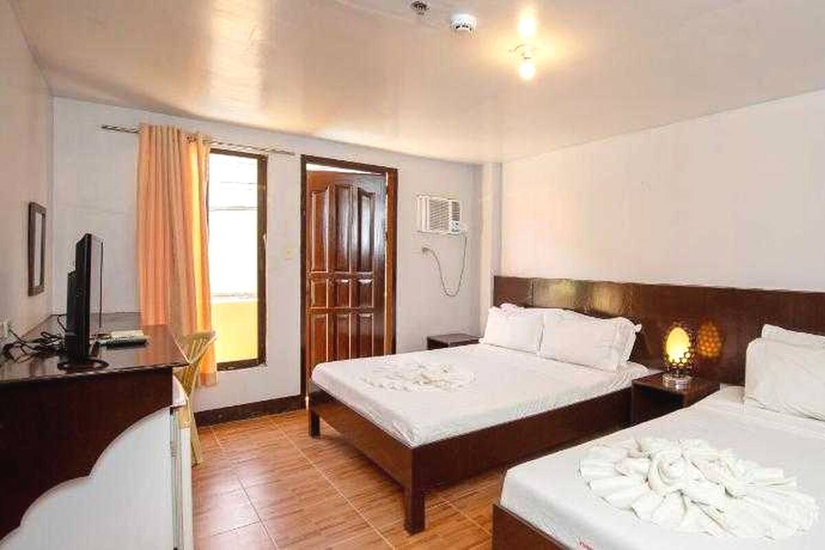 Habitación de hotel con dos camas, un escritorio, un televisor y aire acondicionado.