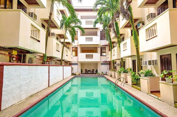 A swimming pool surrounded by multi-story buildings with balconies, some with plants. - Palette Boracay Isle by The White Beach (Boracay Island)